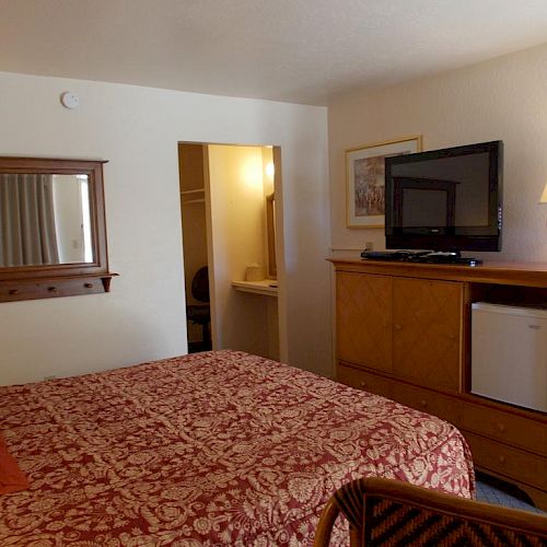 This image shows a hotel room with a bed, a TV on a dresser with a lamp, a fridge beneath, and a wall mirror above.