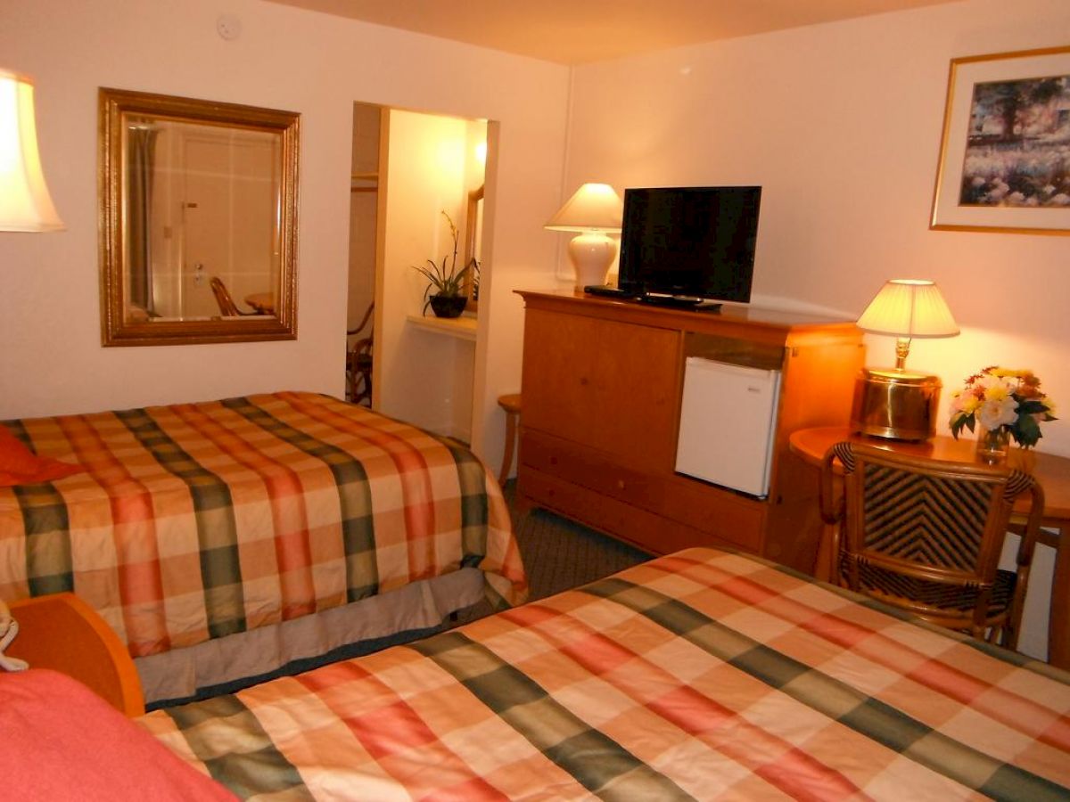 A cozy hotel room with two beds, a wooden dresser, a table and chairs, a flat-screen TV, and warm lighting, giving it a welcoming atmosphere.