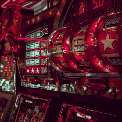 The image shows illuminated slot machines in a dark casino environment, with bright red and neon lights reflecting off the machines.