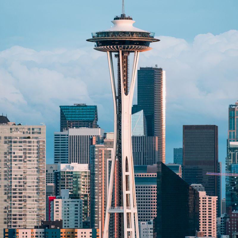 This image shows the Space Needle, an iconic observation tower in Seattle, with surrounding skyscrapers and a cloudy sky in the background.