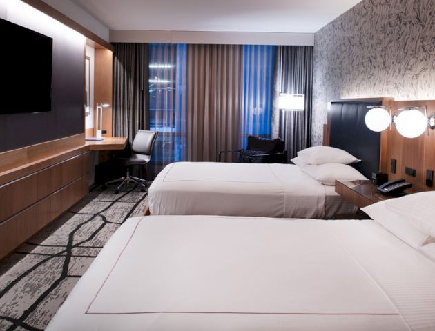 A modern hotel room with two neatly made beds, a desk, a wall-mounted TV, and stylish decor.