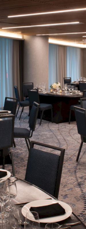 An elegantly set dining room with round tables and chairs, adorned with white flowers, glassware, and black napkins, featuring modern lighting.