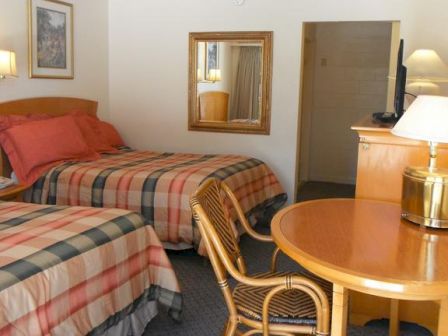 A hotel room with two beds, a table and chair, a mirror, and a TV on a wooden dresser. The beds have plaid bedspreads.